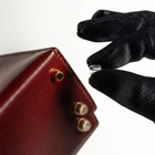 Hand wearing a black glove holding a small object near a brown leather Dear Bag wallet on a white background